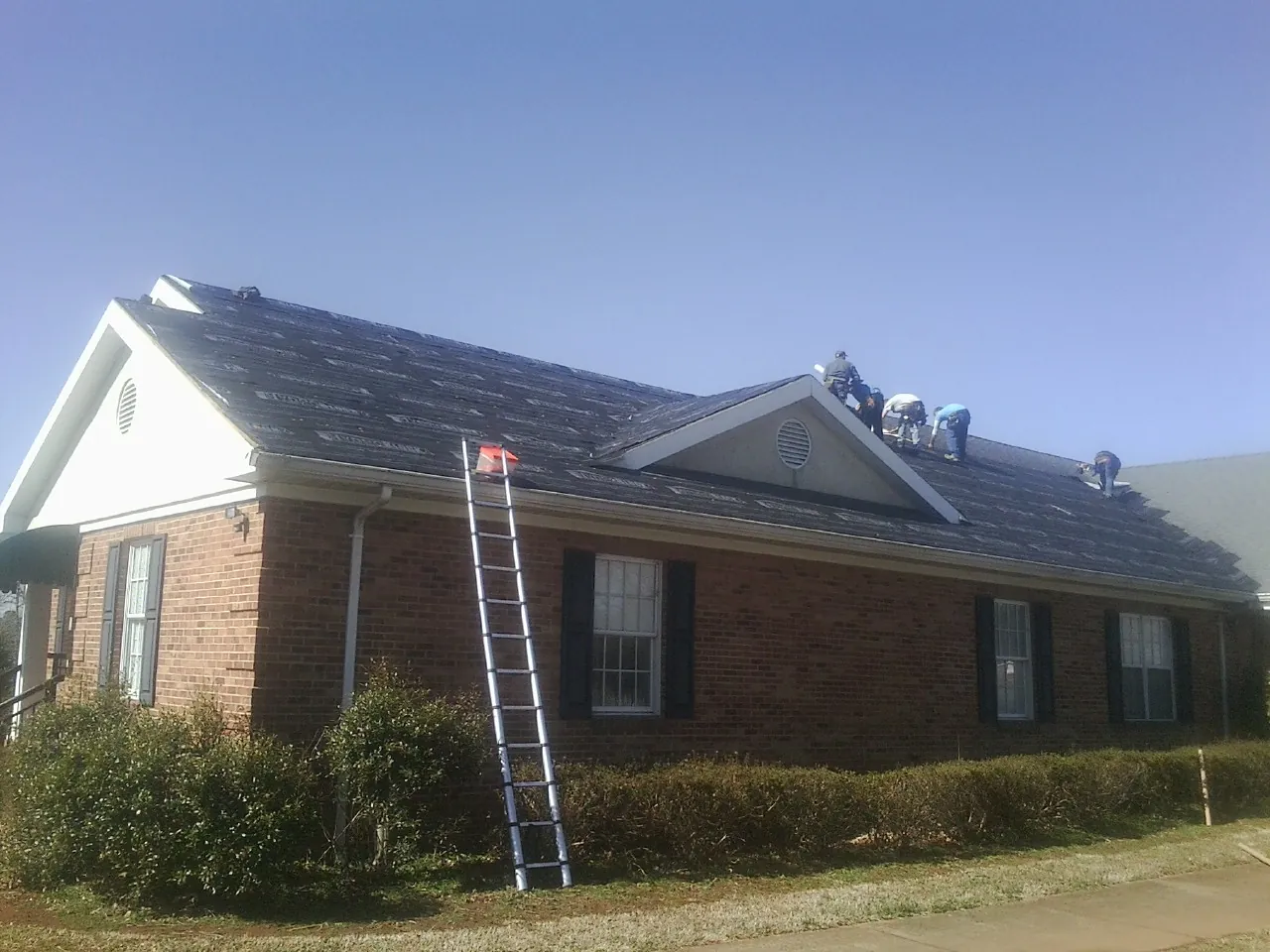 Crew tearing shingles off a brick ranch roof with a ladder set — Metal Roof Repair work by our crew in Millers Falls