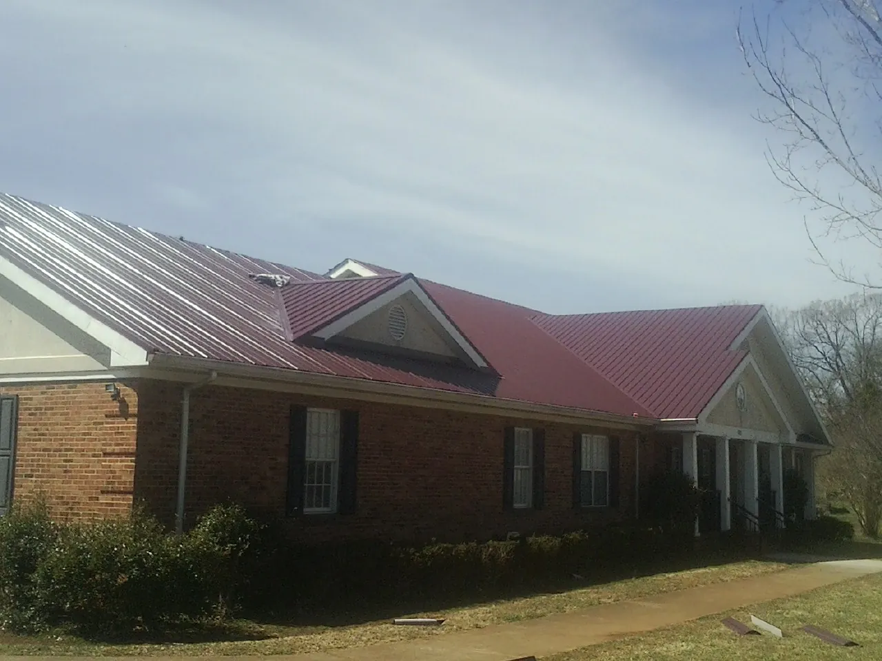 Red metal roof with gabled entries on a long brick building, from a Hail Damage Roof Repair job in Millers Falls