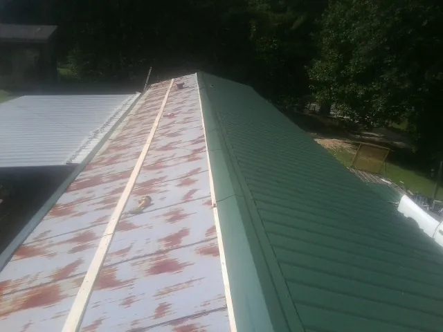 Old rusted panels beside newly installed green metal roofing — Wind Damage Roof Repair by Roofing Brothers in Millers Falls