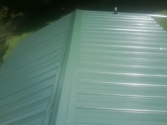 New green metal panels meeting at the ridge of a roof — Flat Roof Repair work by our crew in Millers Falls