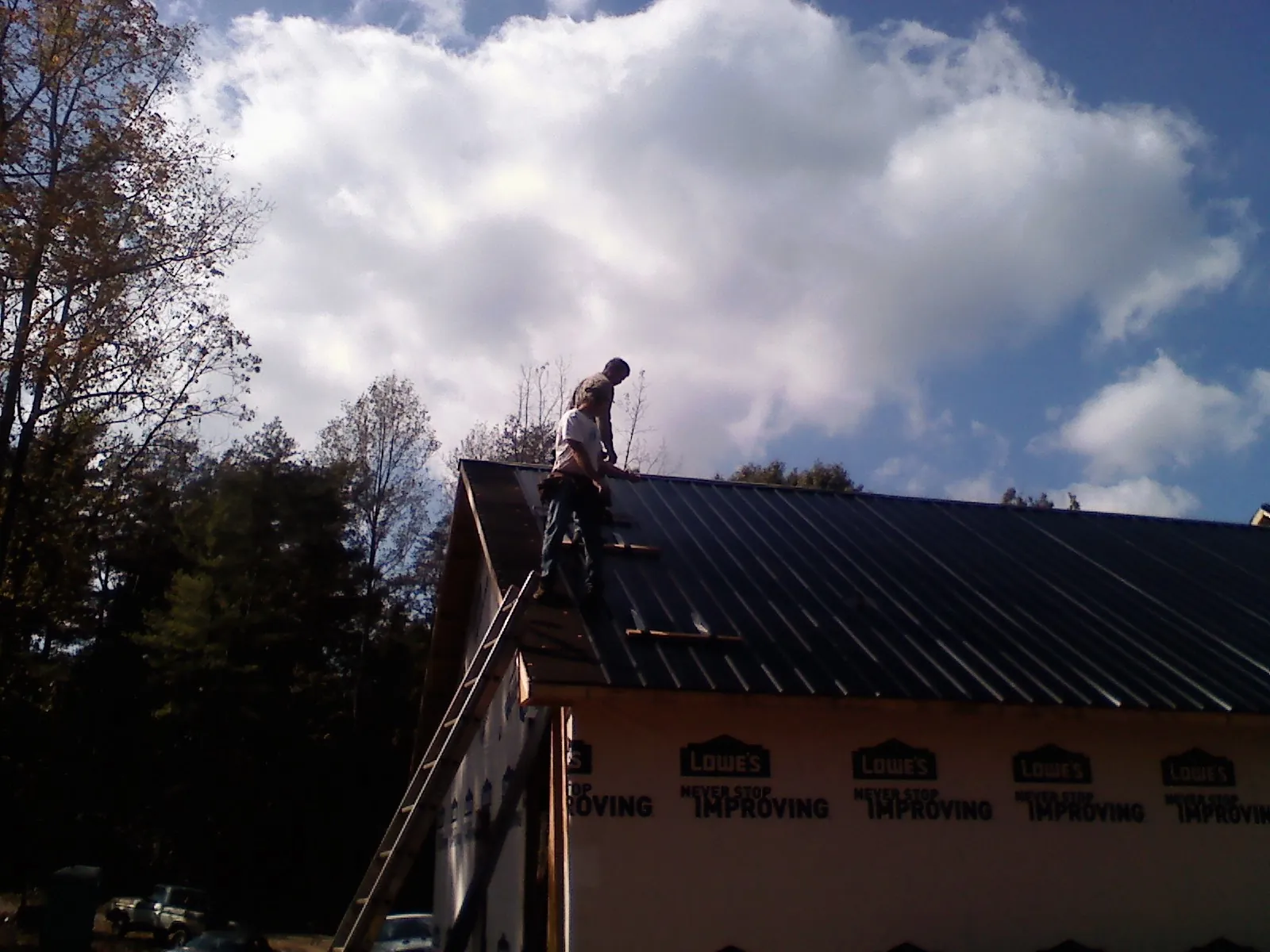 Roofer fastening dark metal panels high against a cloudy sky, from a Roof Inspection job in Millers Falls