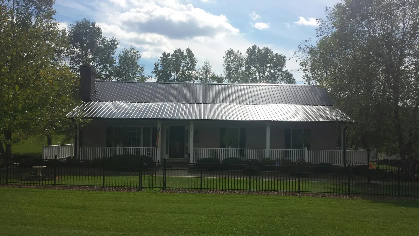Gray metal roof on a brick ranch with a full width front porch — Gutter Guard Installation work by our crew in Millers Falls