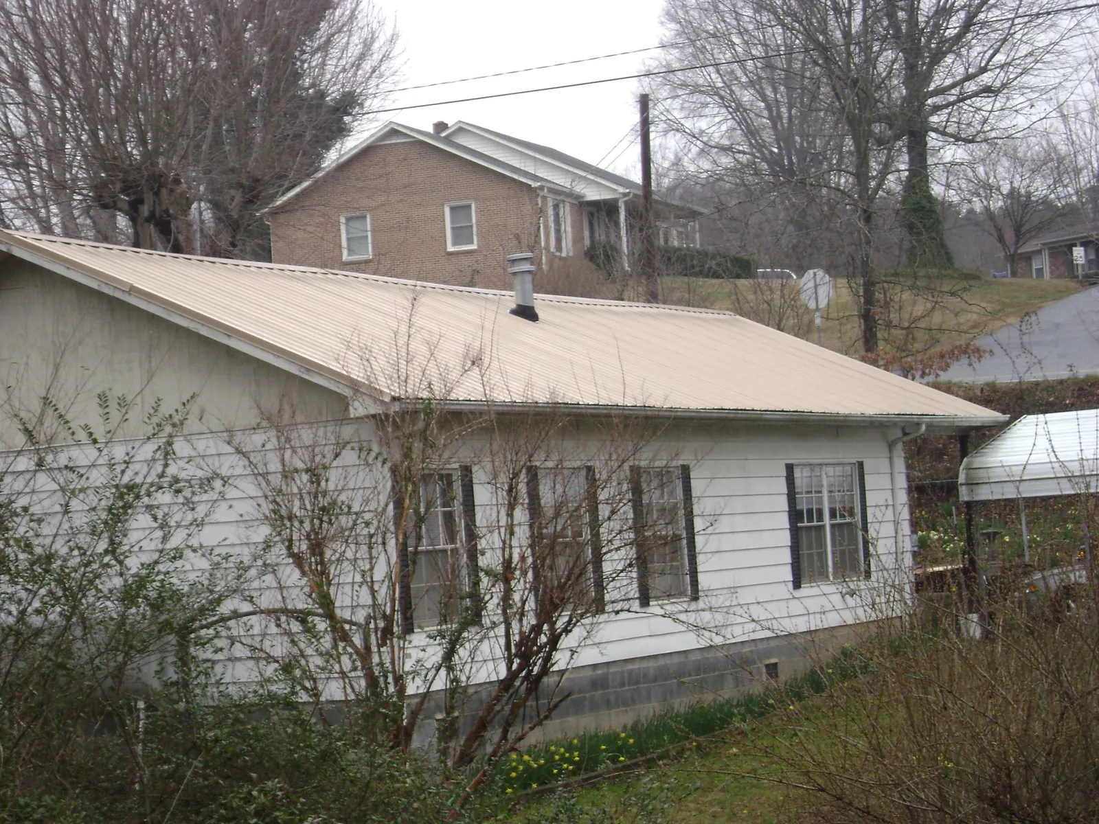 Tan metal roof on a white sided house set into a hillside — Commercial Roofing by Roofing Brothers in Millers Falls