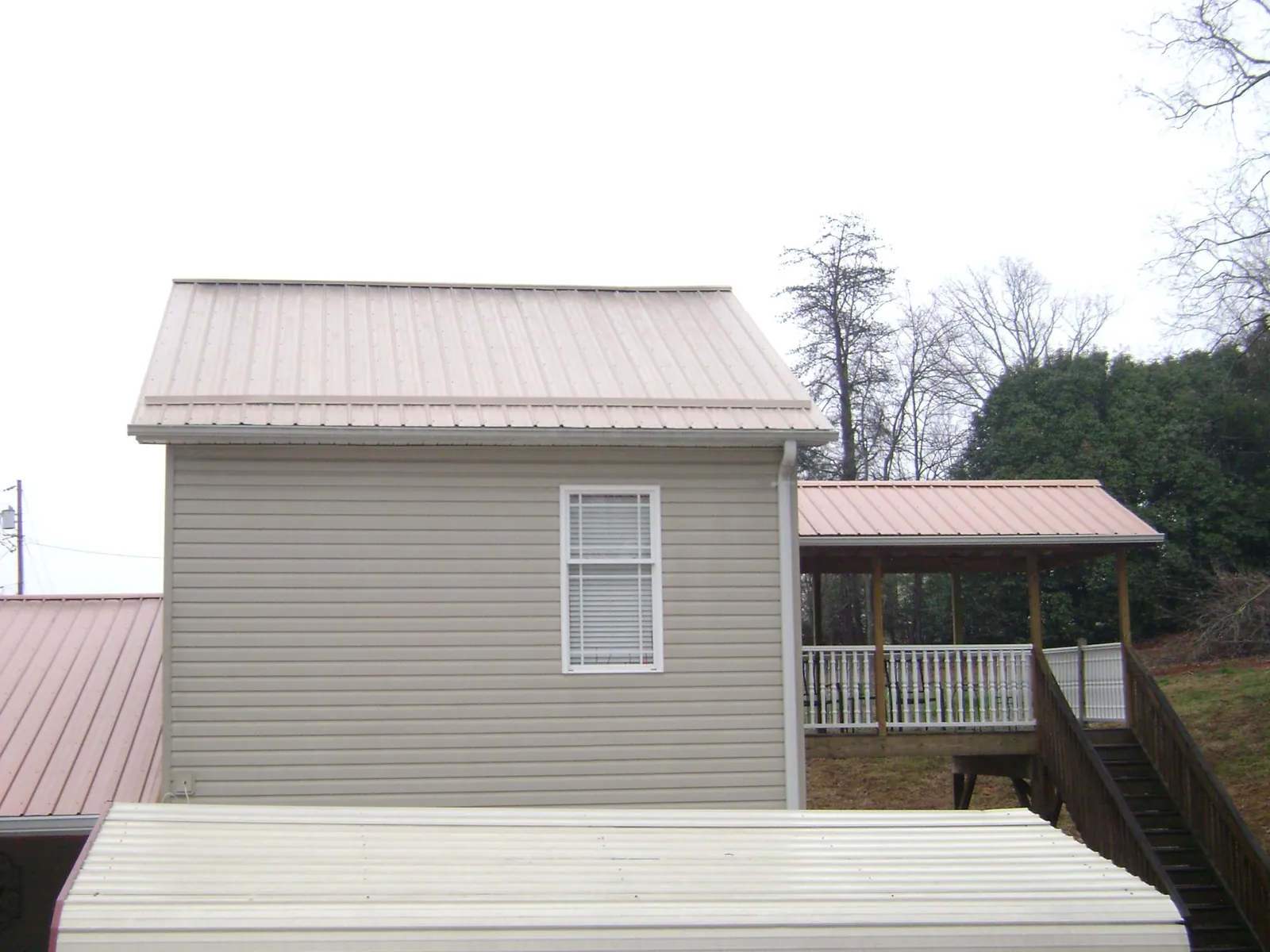 Tan metal roofs on a two story addition and attached porch, from a Roof Replacement job in Millers Falls