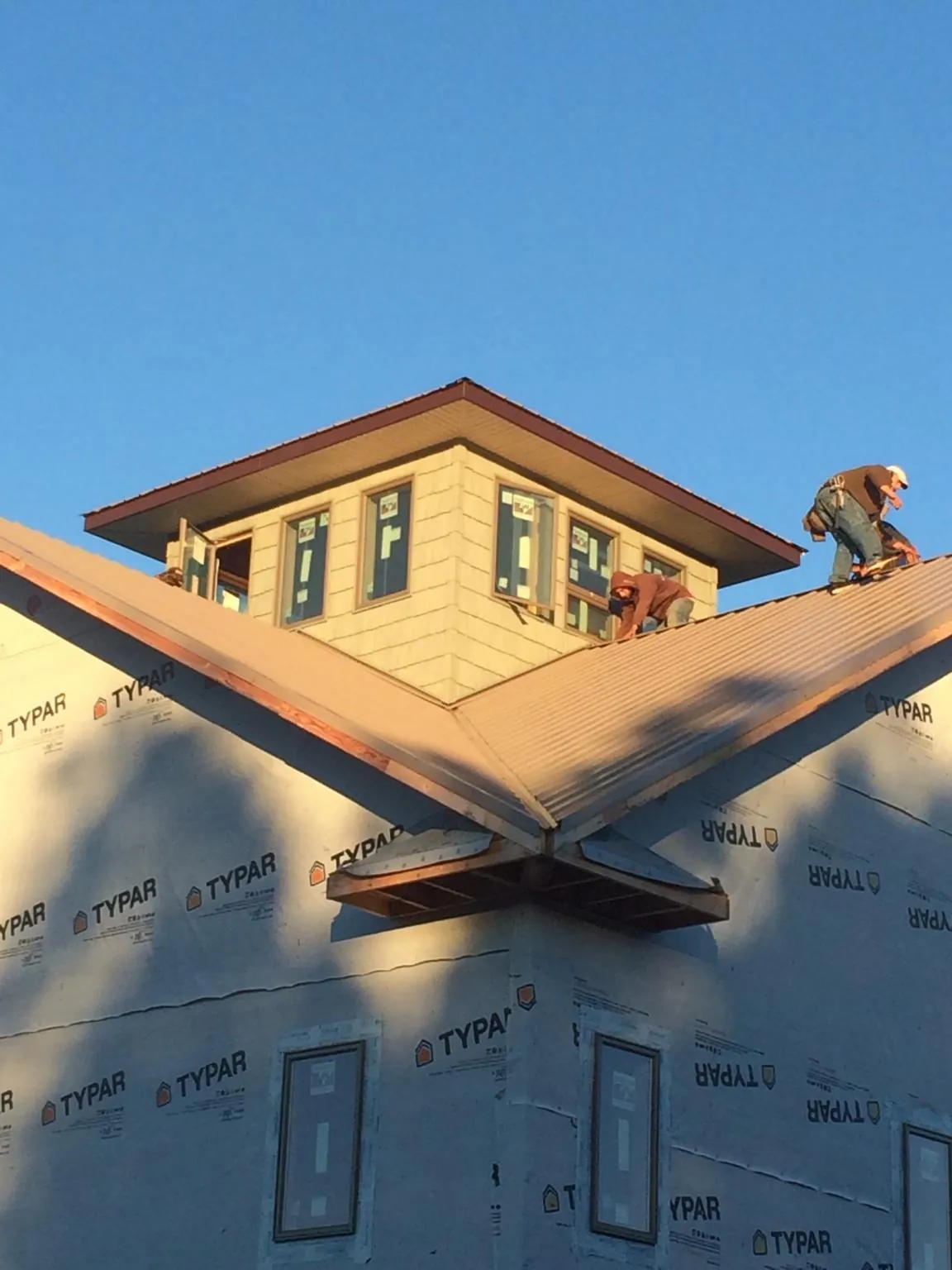 Roofers working around a rooftop cupola on a new metal roof at sunset — Roof Waterproofing in Millers Falls by Roofing Brothers